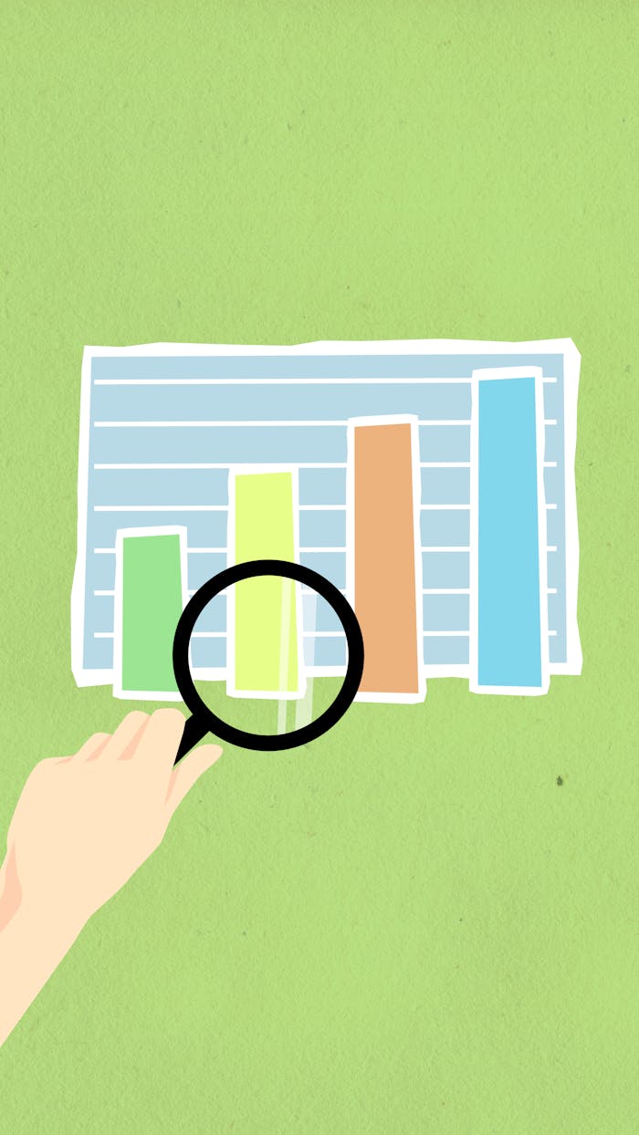 Top view of decorative cardboard illustration of hand with magnifying glass above diagram with columns on green background